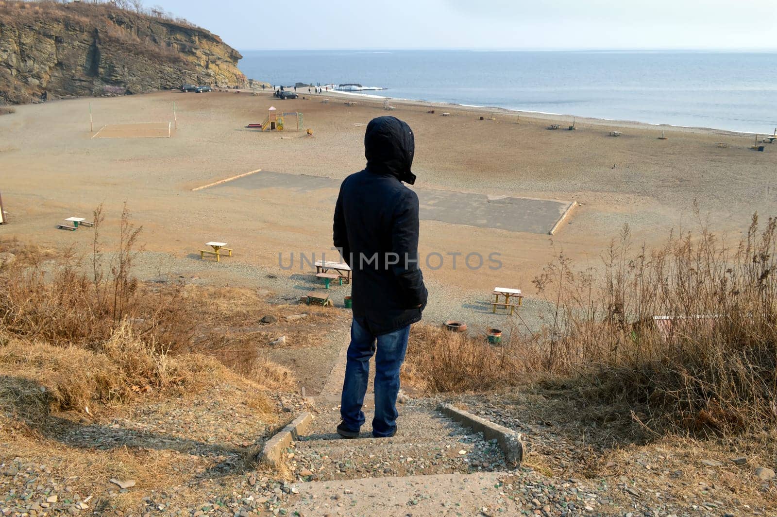 Upset man standing in black jacket on destroyed stairs and looking at Japanese sea on an autumn day
