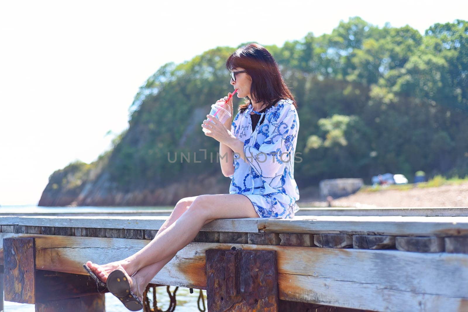 45 years old Russian woman drinking lemonad and sitting on pier
