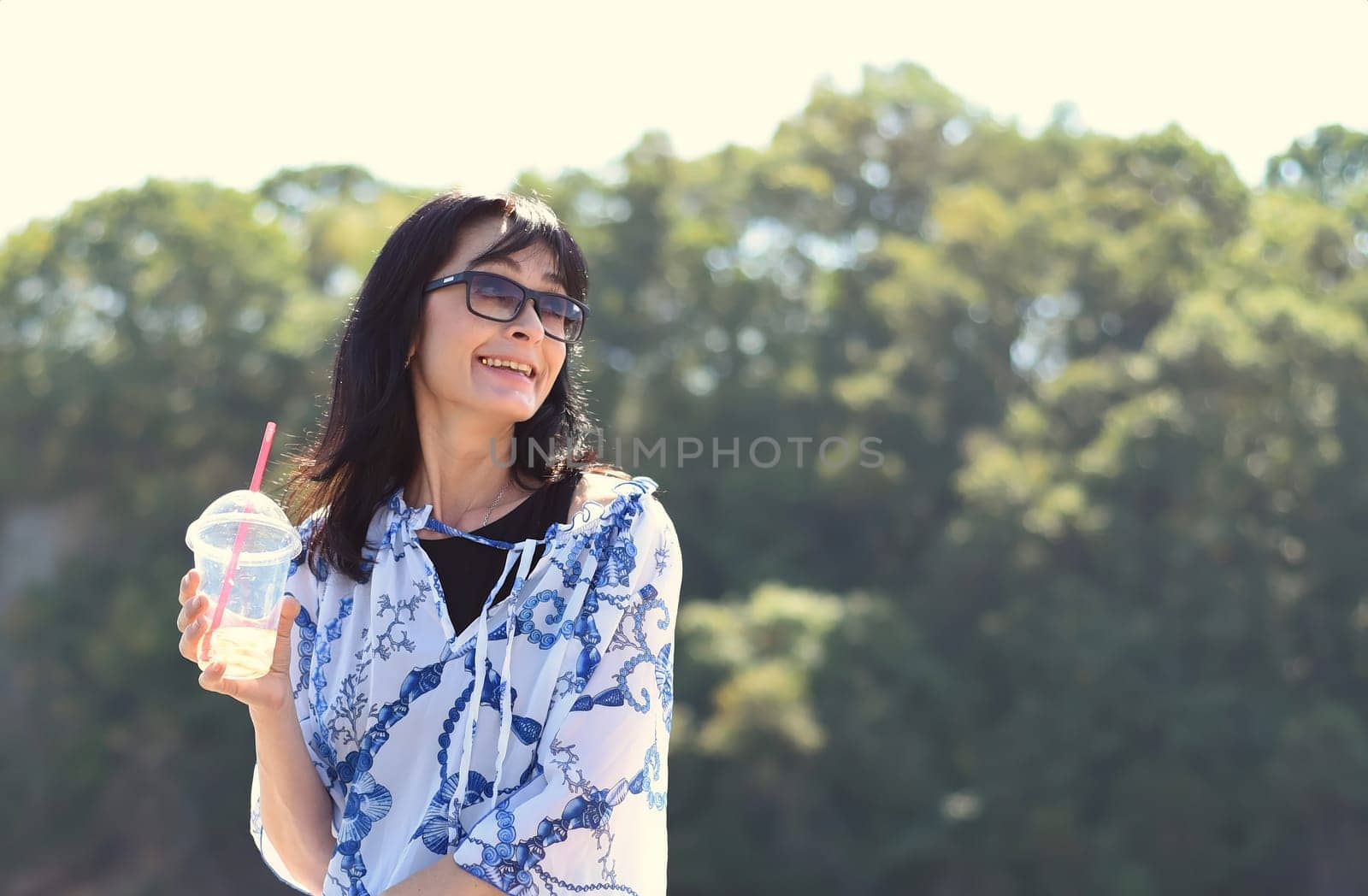 45 years old Russian woman drinking lemonade and sitting on pier