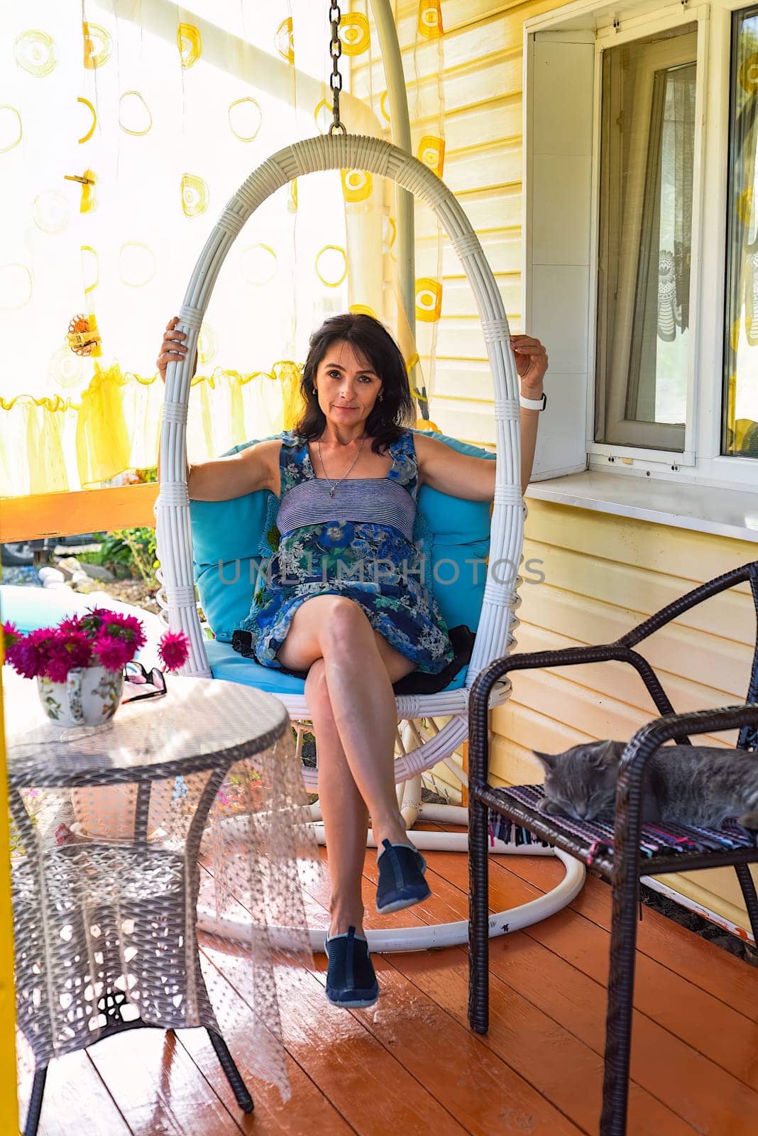 45 years old Russian woman resting on hanging swing chair on cozy veranda with slepping cat