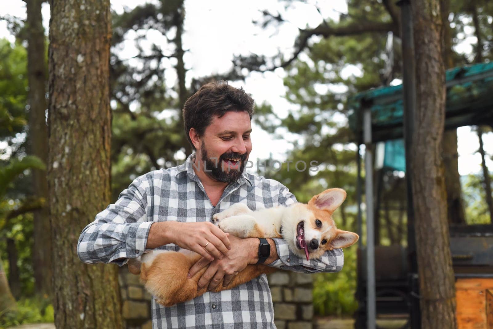 Happy bearded man holding his welsh corgi dog and smiles