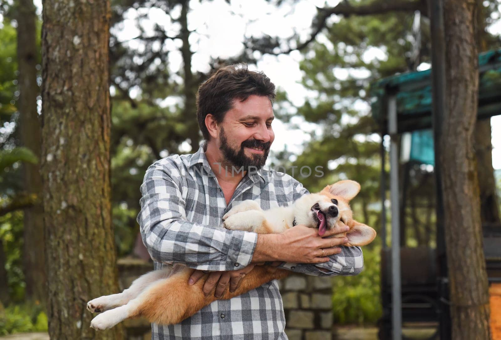 Happy bearded man holding his welsh corgi dog and smiles
