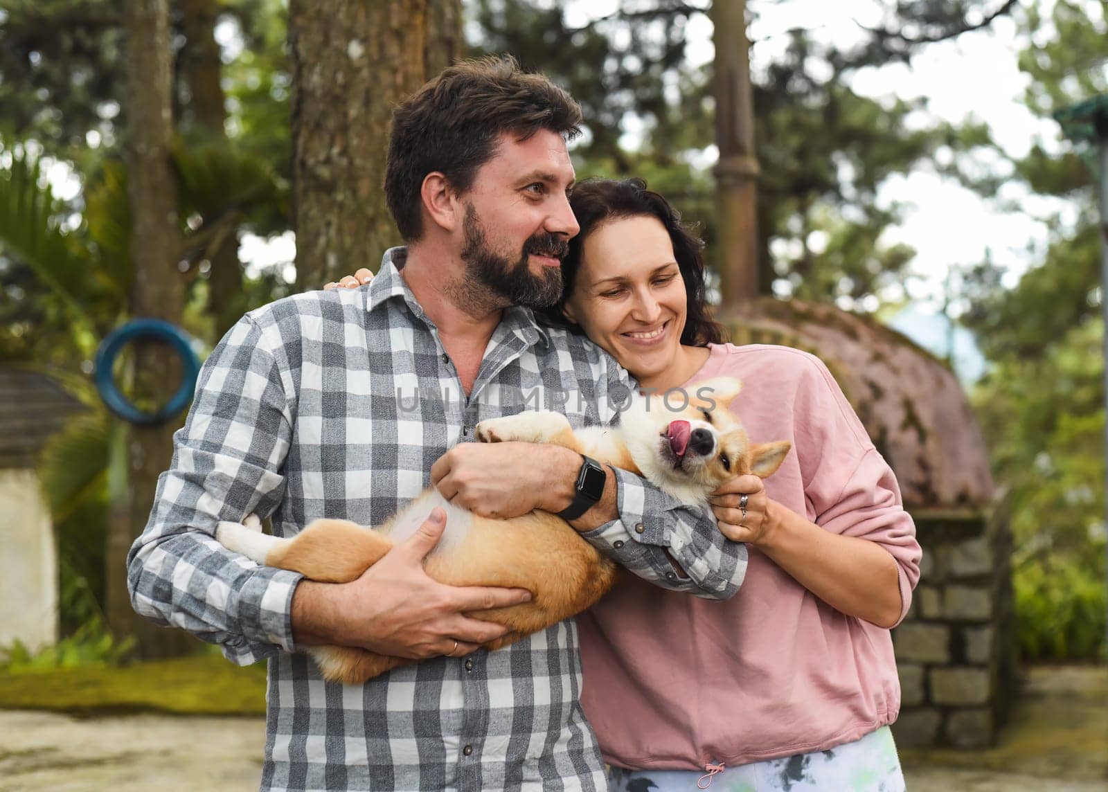 Happy bearded man and woman holding their welsh corgi dog and smiling