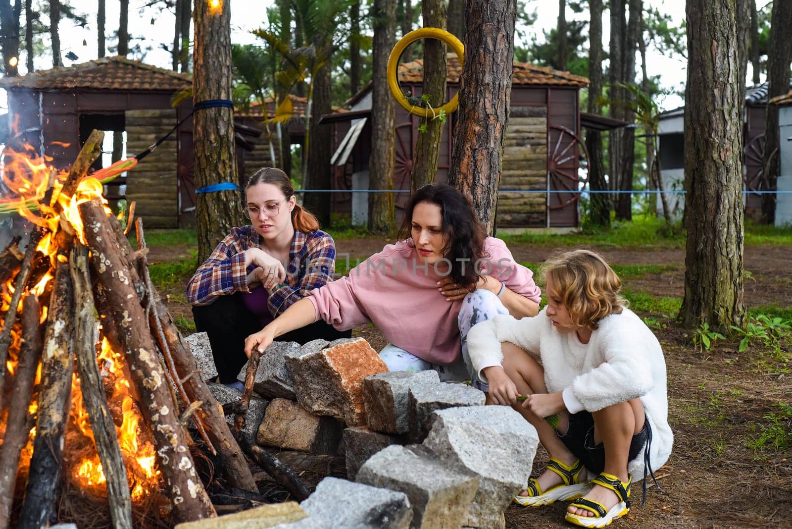 Mother with her daughters spending time together, kindle a fire and throw sticksMother with her daughters spending time together, kindle a fire and throw sticks