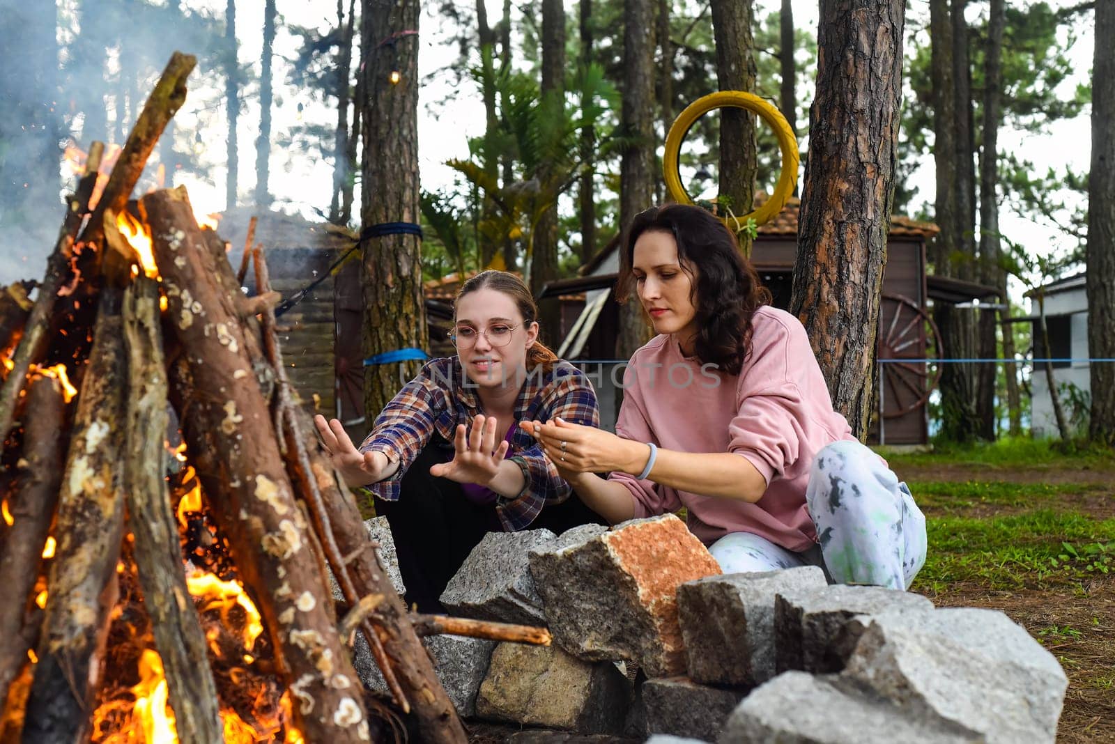 Mother with her daughters spending time together, kindle a fire and throw sticks