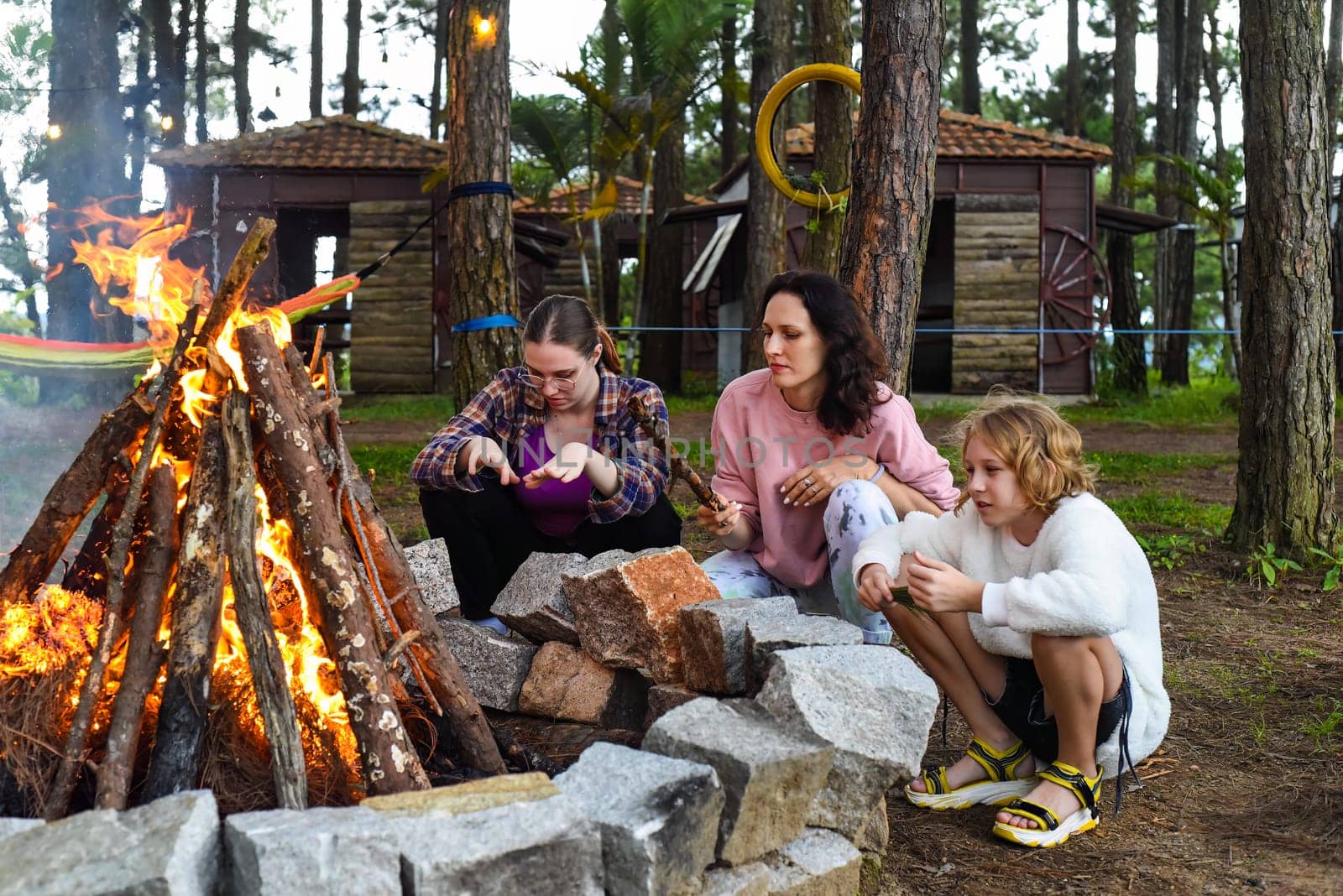 Mother with her daughters spending time together, kindle a fire and throw sticksMother with her daughters spending time together, kindle a fire and throw sticks