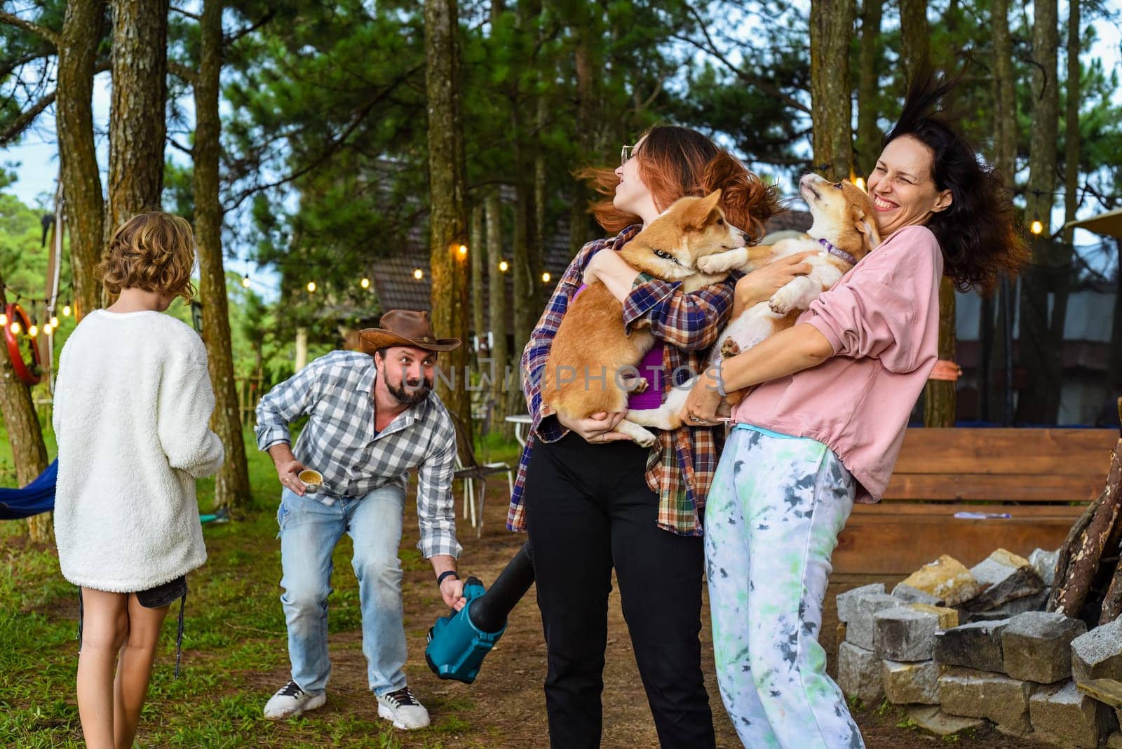 Funny family moment with father using garden blower for teasing his wife and daughter holding dogs
