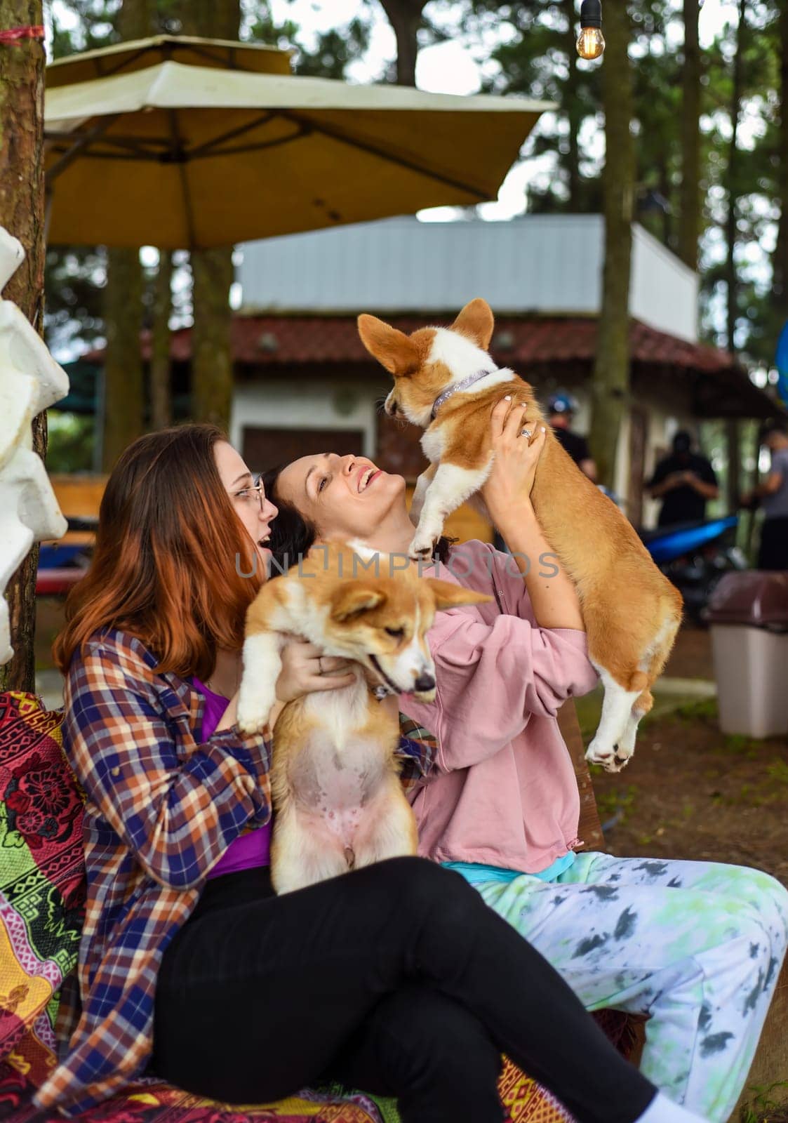 mother with her daughter hugging their corgi dogs in the garden