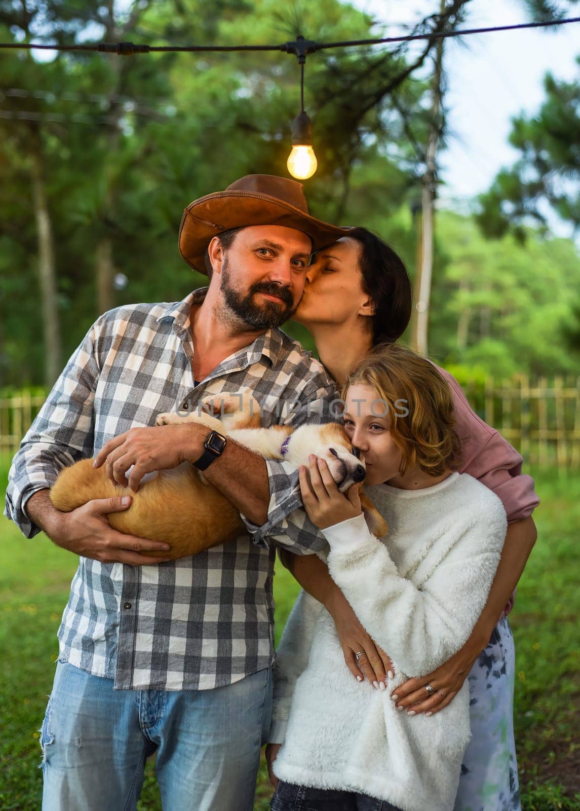Wife kissing her husband and their daughter kissing the corgi dog