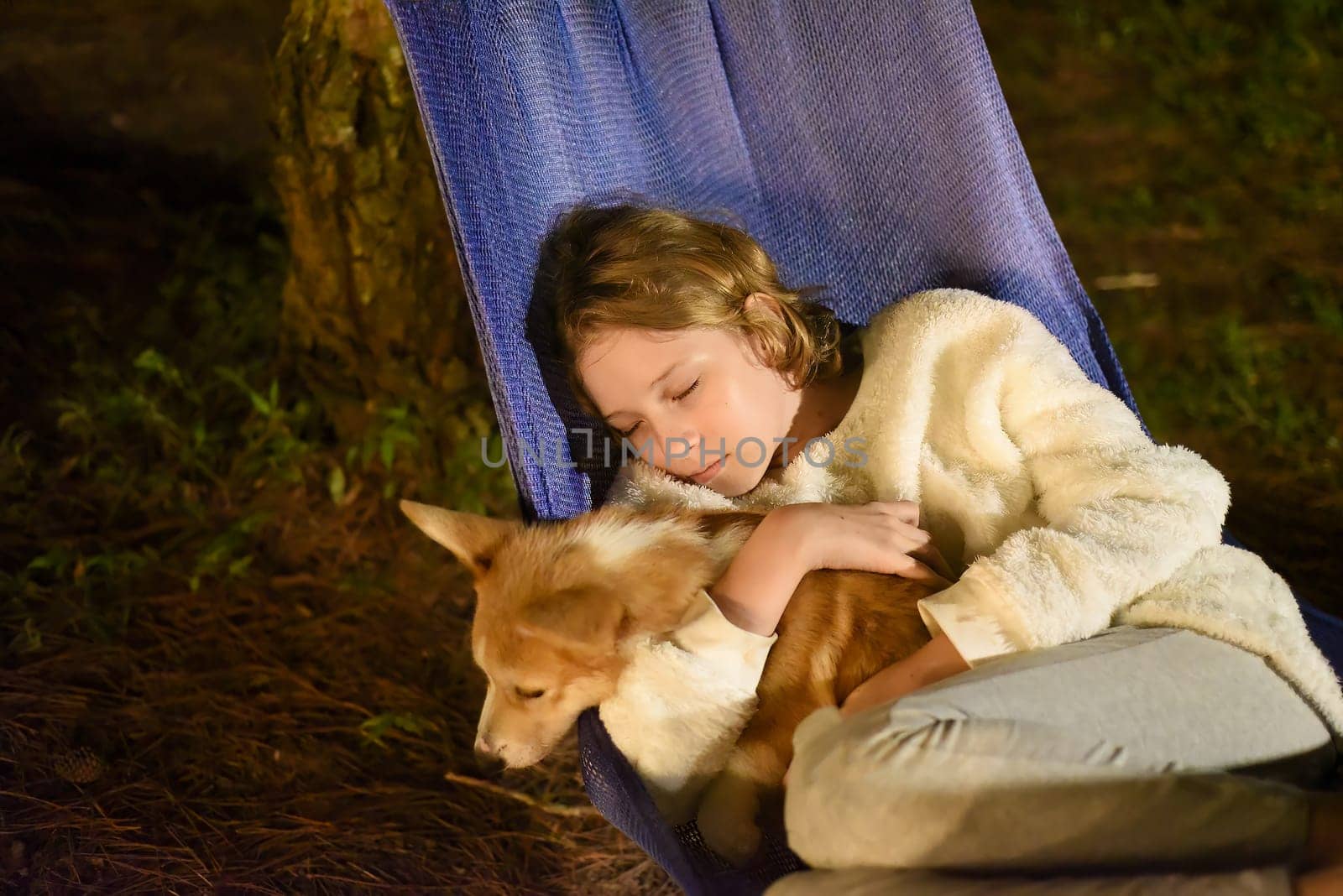 Cute little girl child sleeping in hammock and holding a corgi dog together in camping trip
