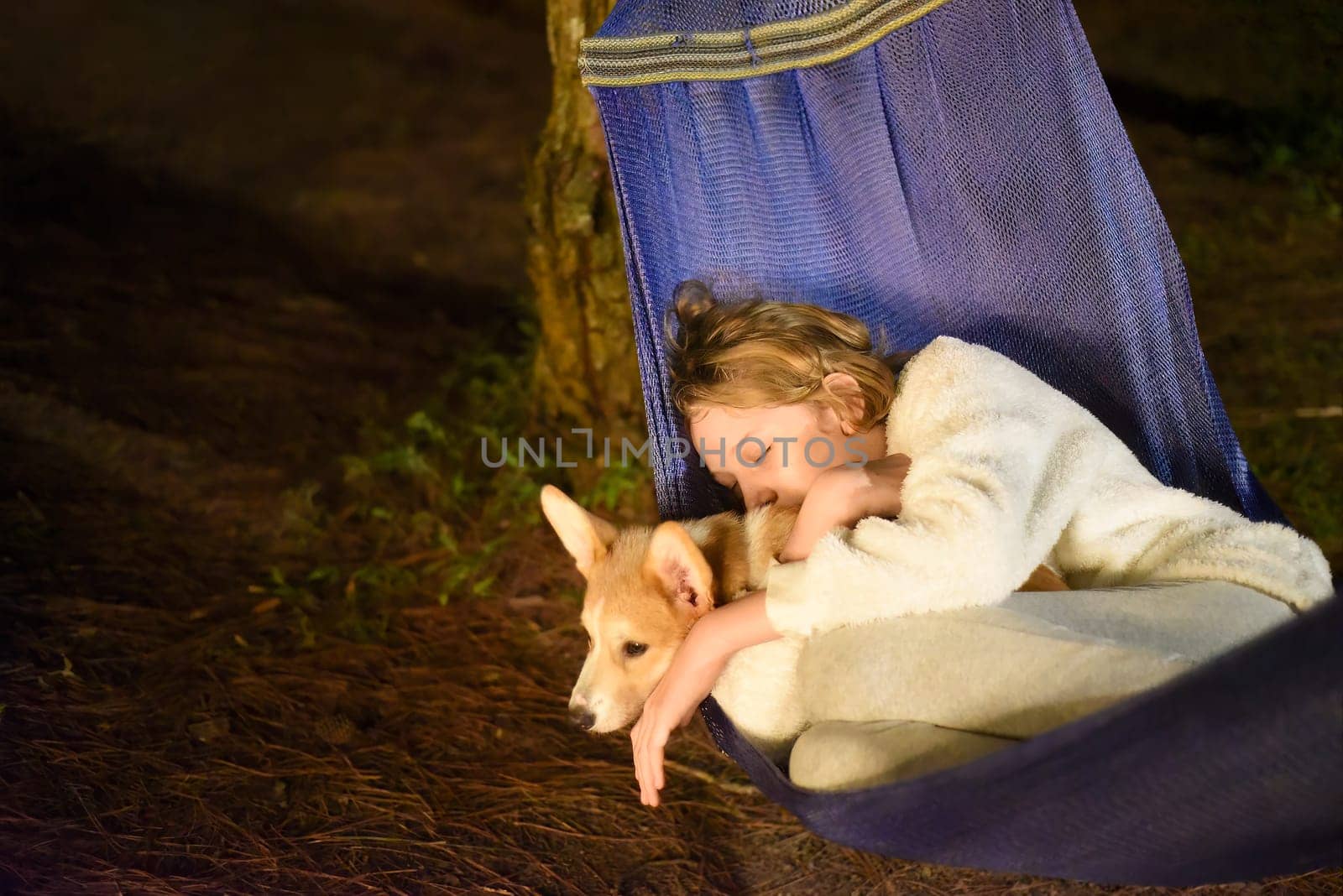 Cute little girl child sleeping in hammock and holding a corgi dog together in camping trip