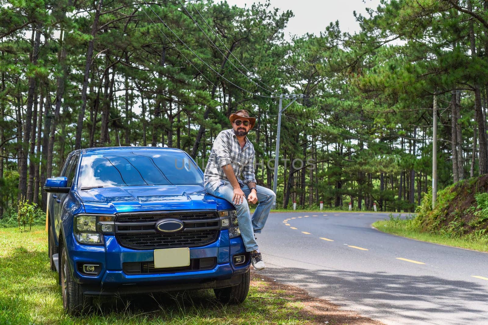 Young man sitting on his blue car in the forest