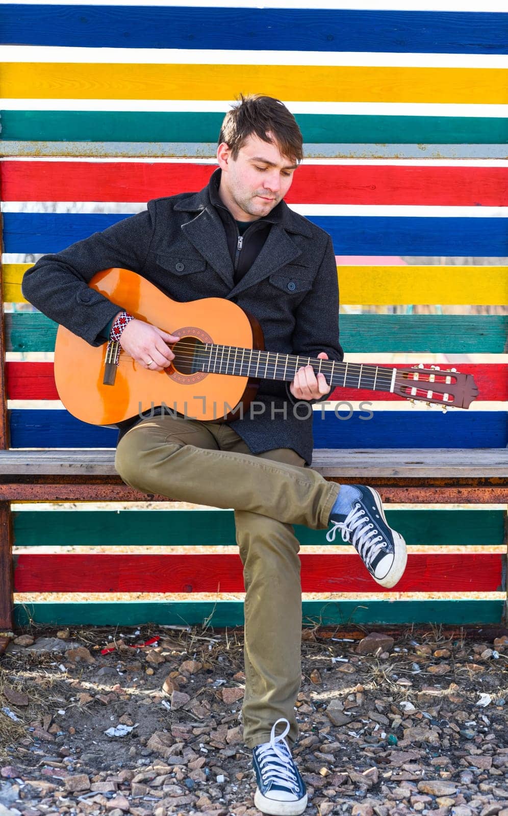 Smiling young man playing guitar and sitting against colorful wall