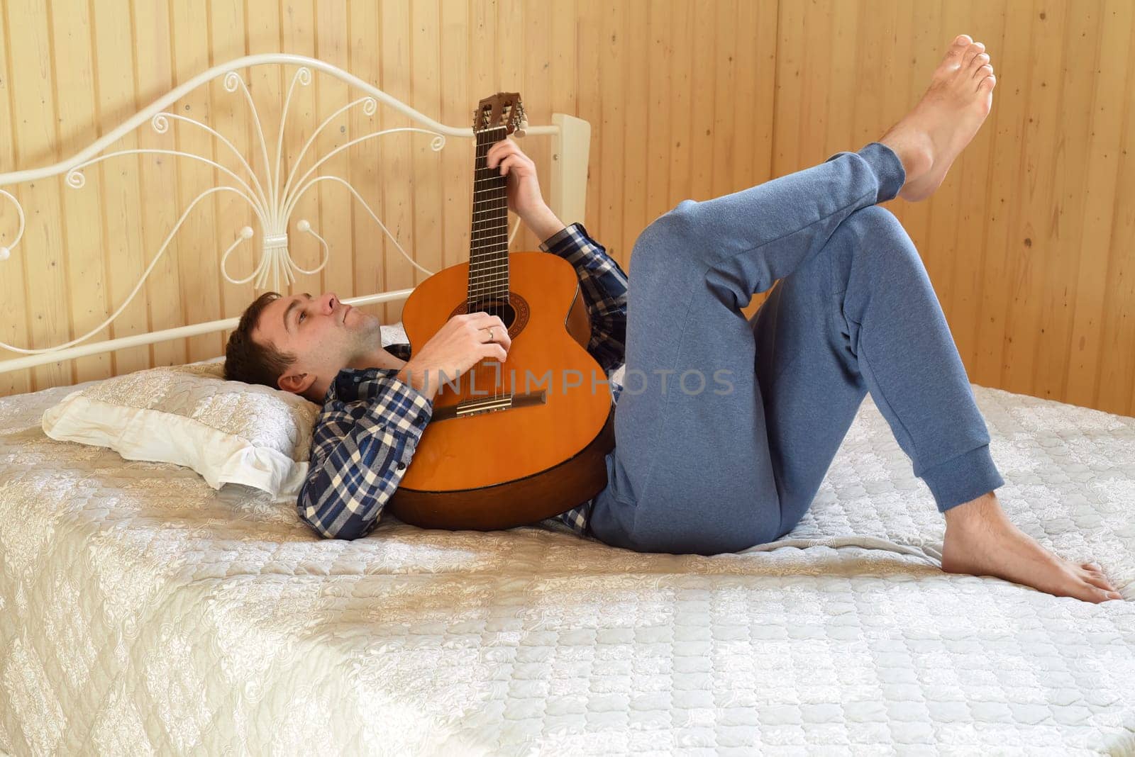 Young man playing guitar and laying on bed on weekend morning