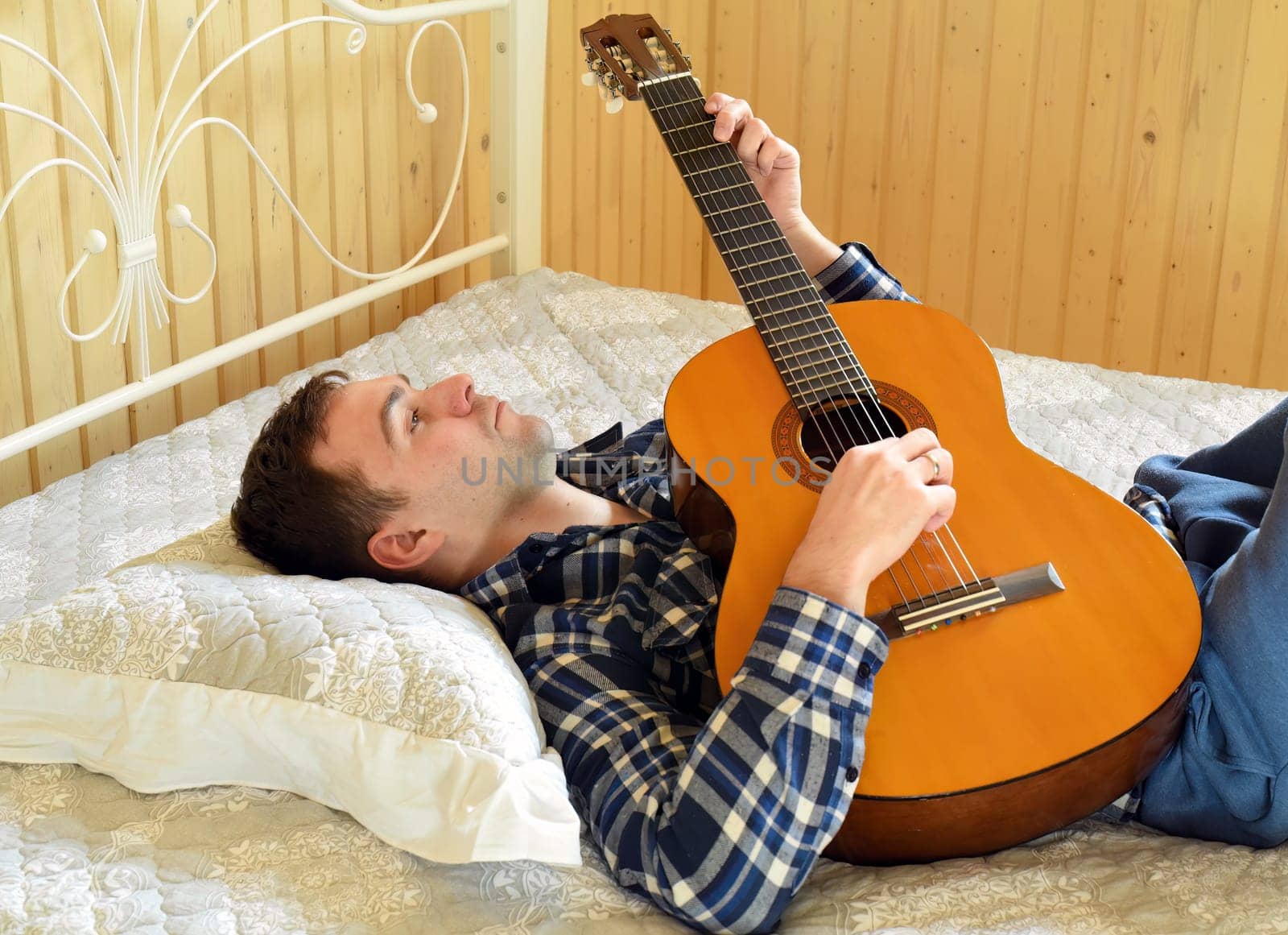 Young man playing guitar and laying on bed on weekend morning