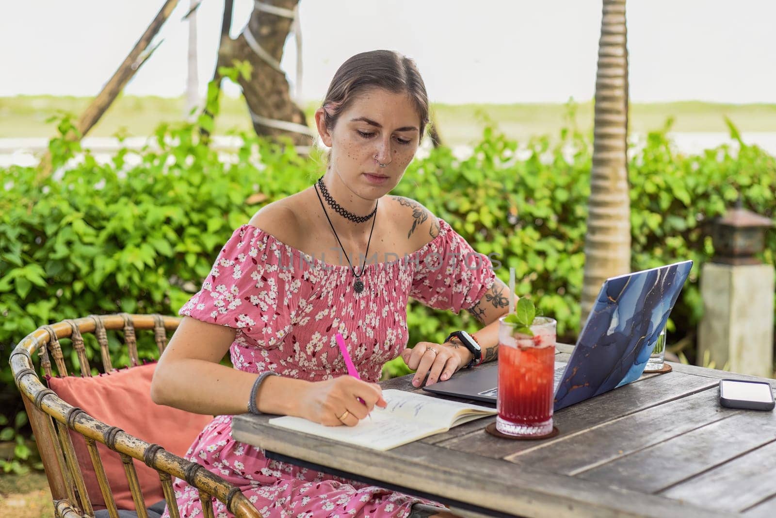 Cute  woman sitting on a chair in summer garden and writing in a notebook