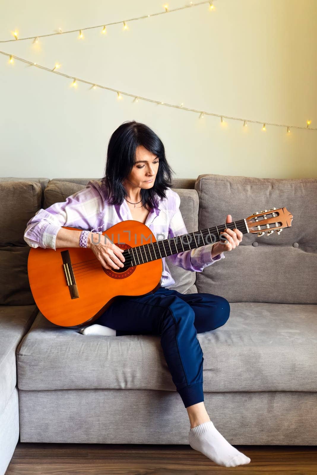 45 y.o. Russian woman playing guitar, sitting on a sofa at home.