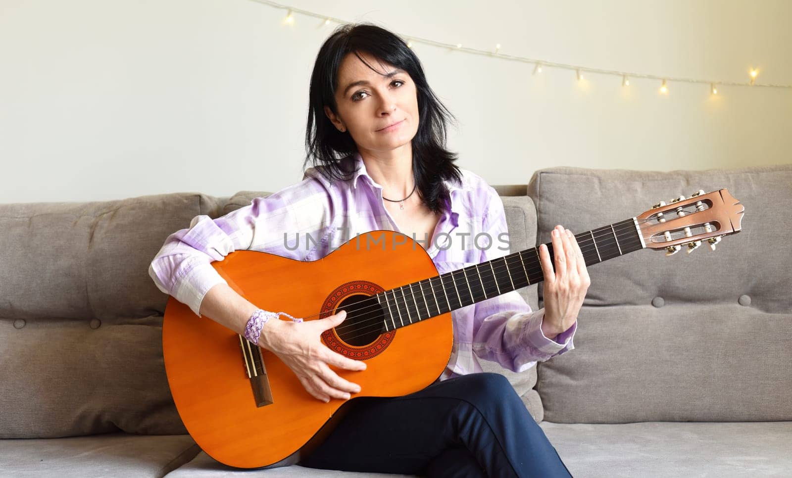 45 y.o. Russian woman playing guitar, sitting on a sofa at home.