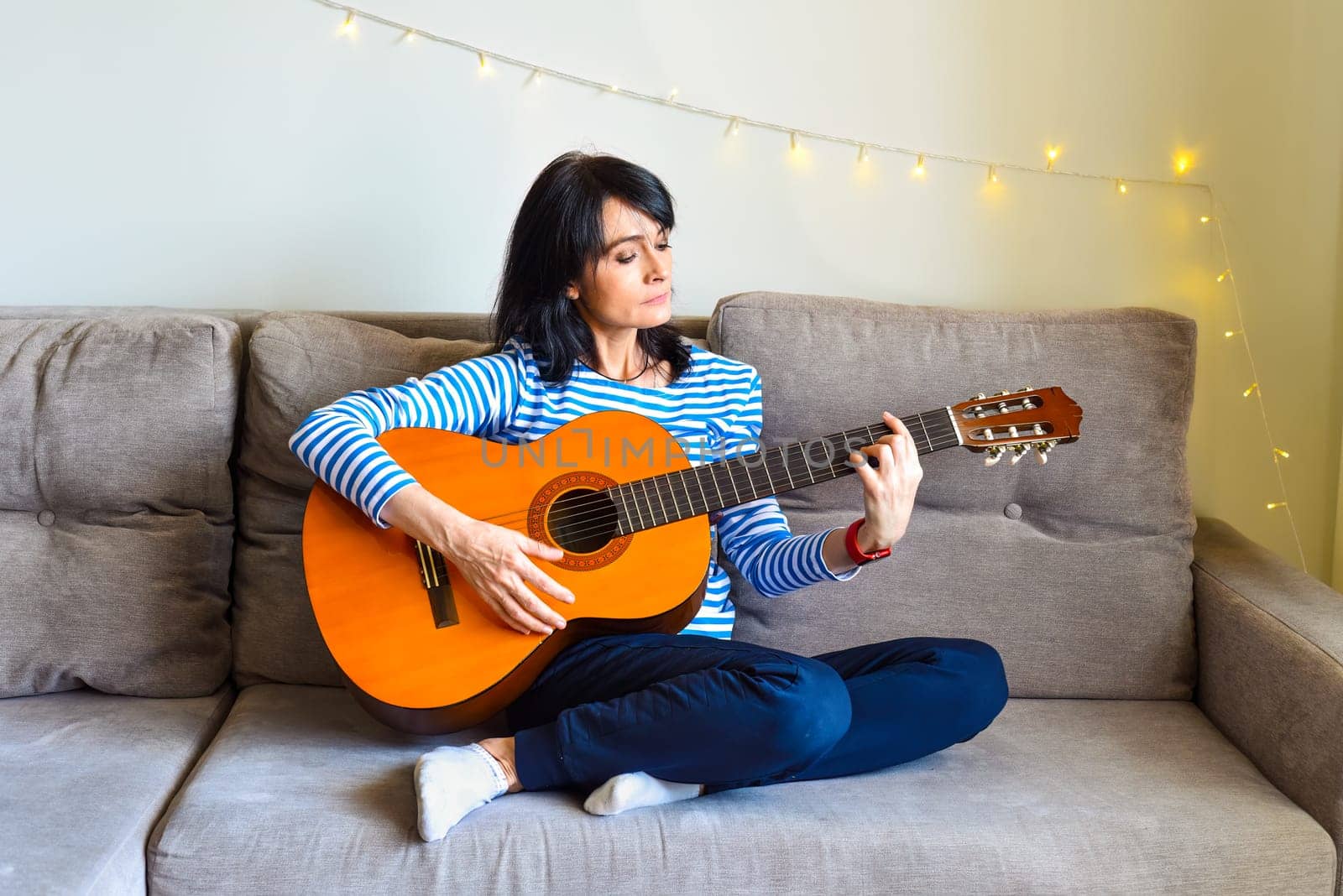 45 y.o. Russian woman playing guitar, sitting on a sofa at home.