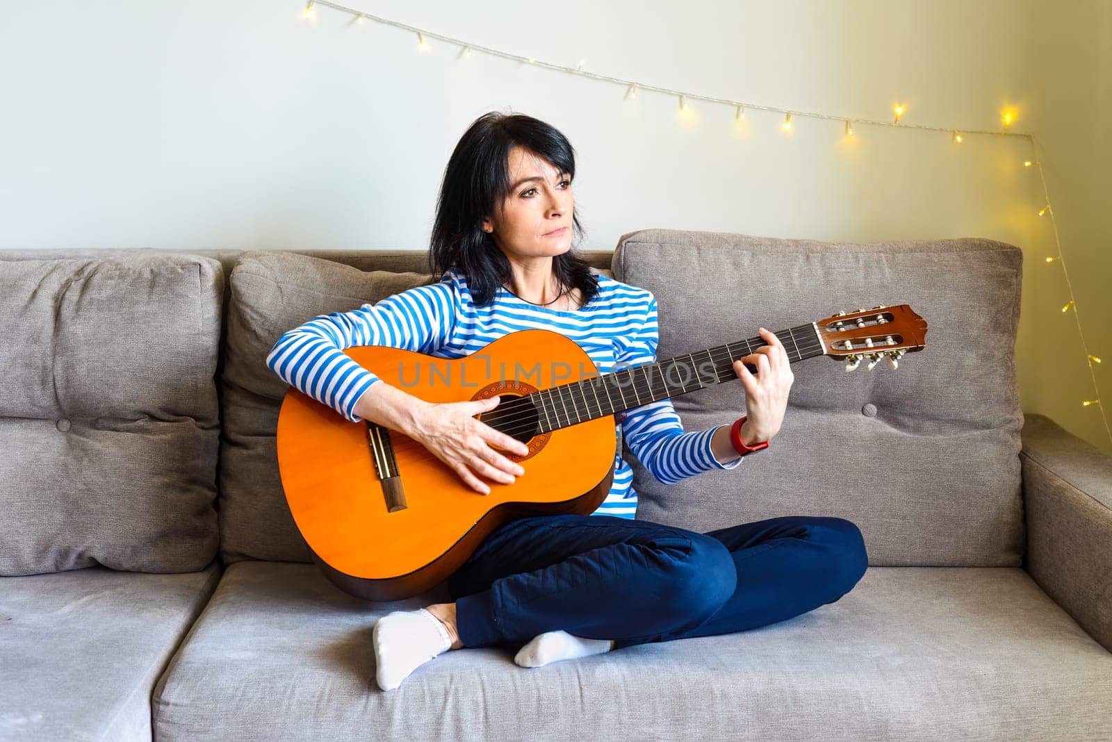 45 y.o. Russian woman playing guitar, sitting on a sofa at home.