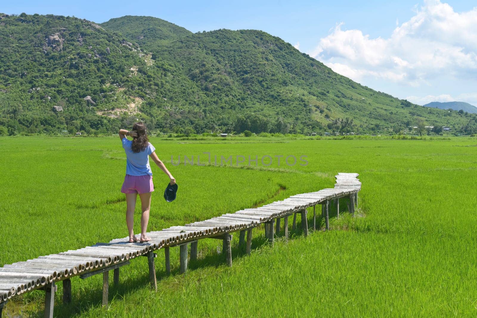A young woman walking across wooden pier in a rice field