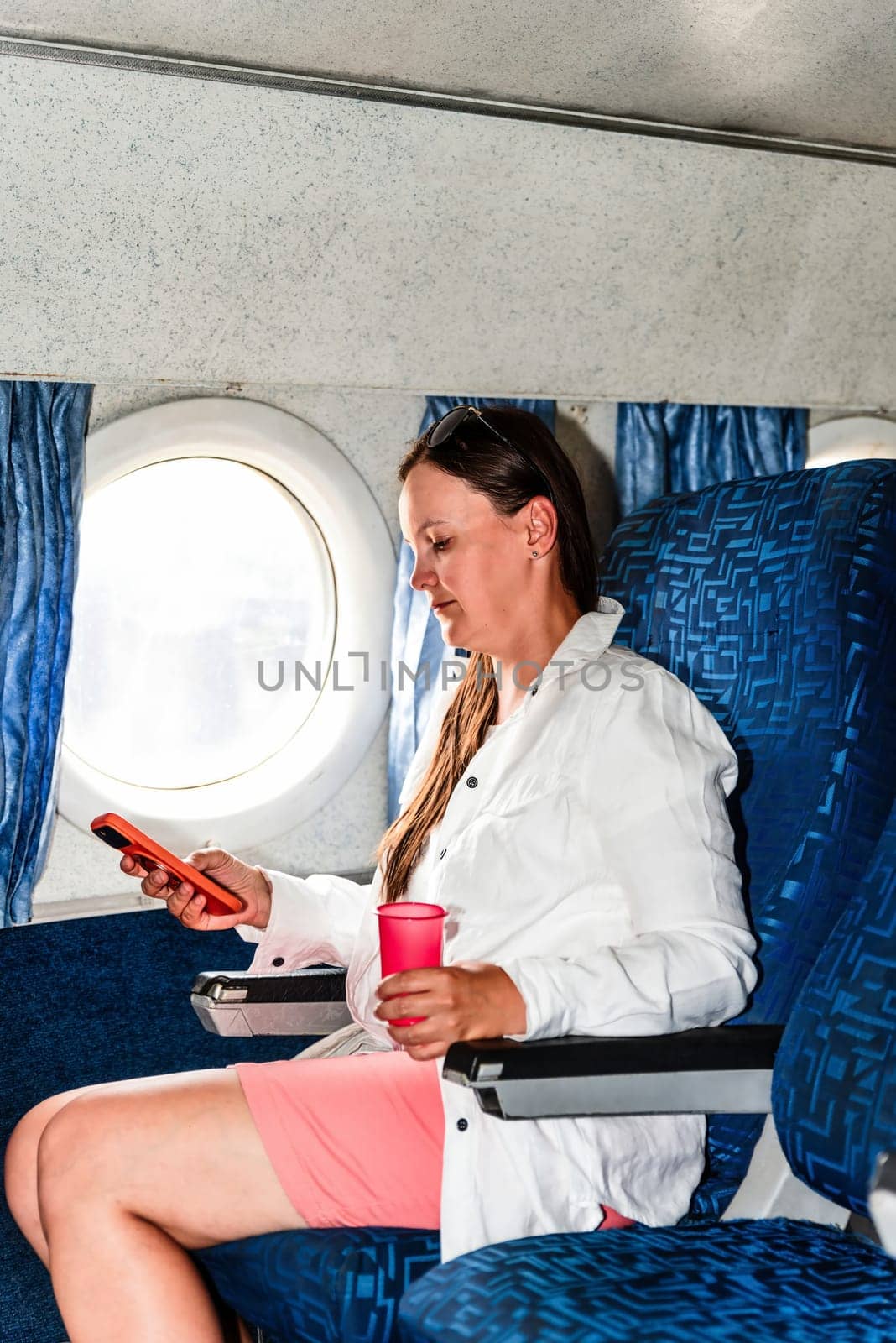 36 years old woman passenger scrolling phone, during a flight in the airplane cabin