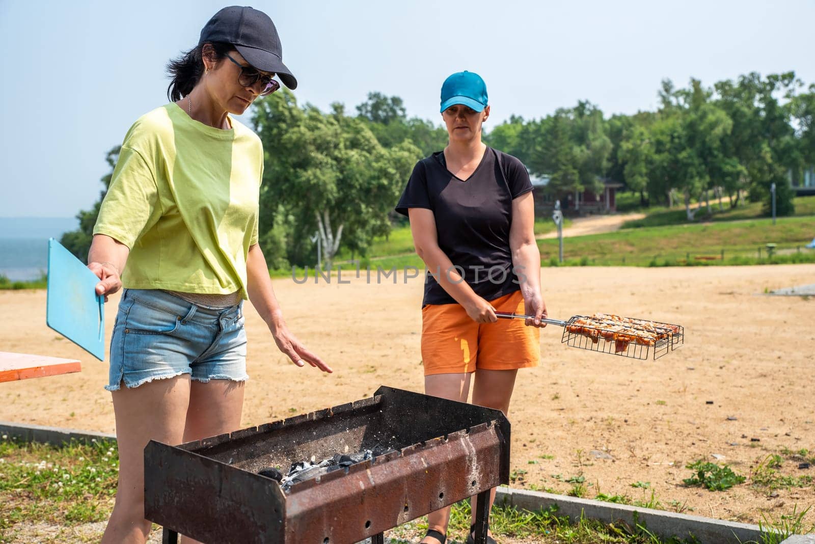 Two russian woman talking and cooking pork bbq on the beach of Japanese sea in the summer