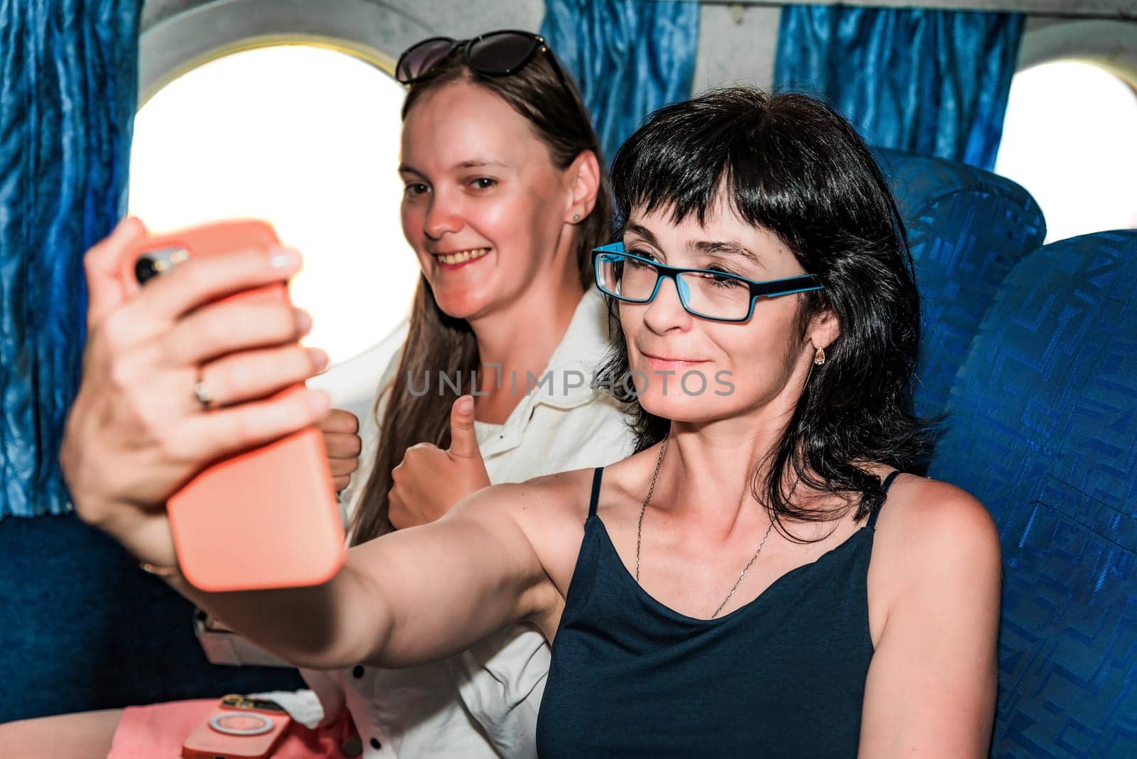 Two beautiful women passengers making a selfie, sitting in the airplane cabin
