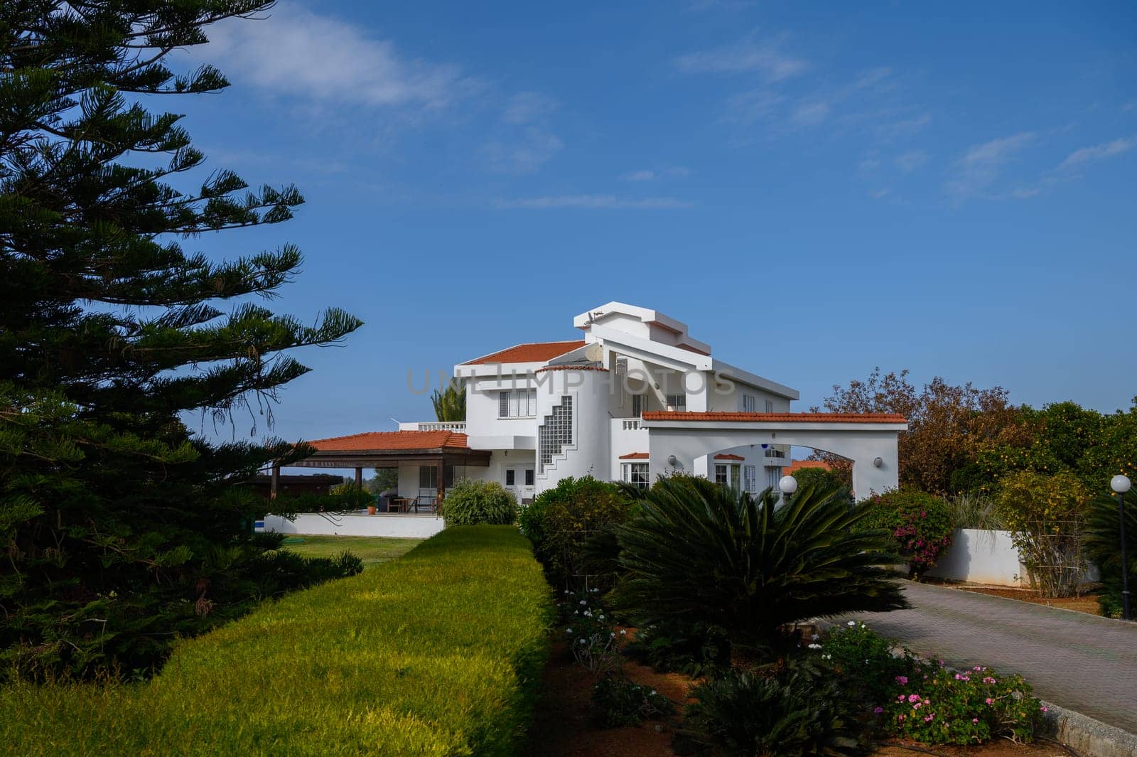 A stunning white villa stands elegantly in the afternoon, surrounded by vibrant greenery and a clear blue sky.
