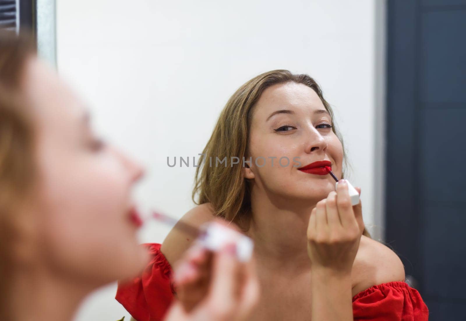 Blond beautiful woman aplying a red lipstick and looking at the mirror