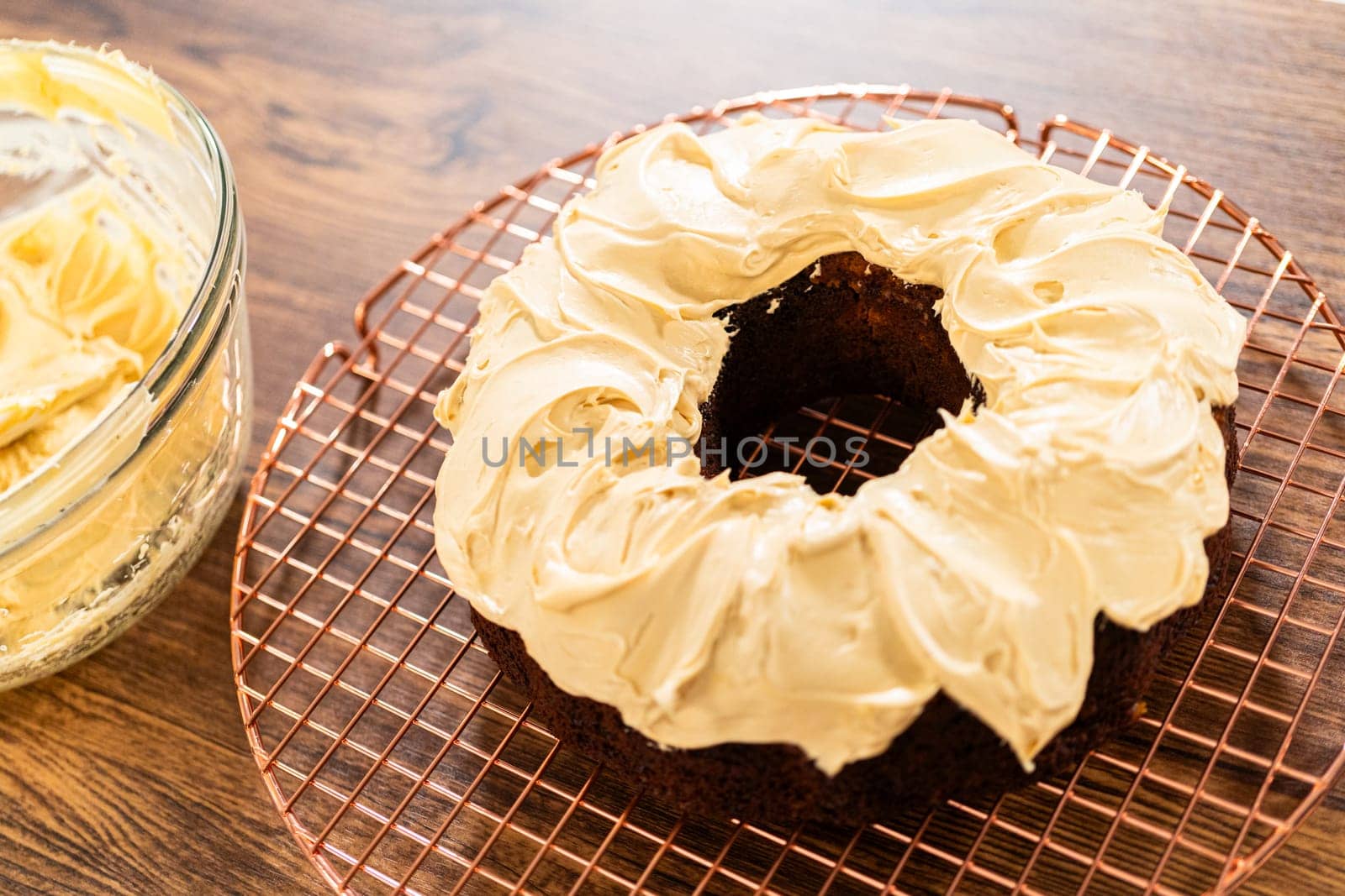 A gingerbread bundt cake being generously frosted with salted caramel frosting and topped with delightful gingerbread sprinkles.