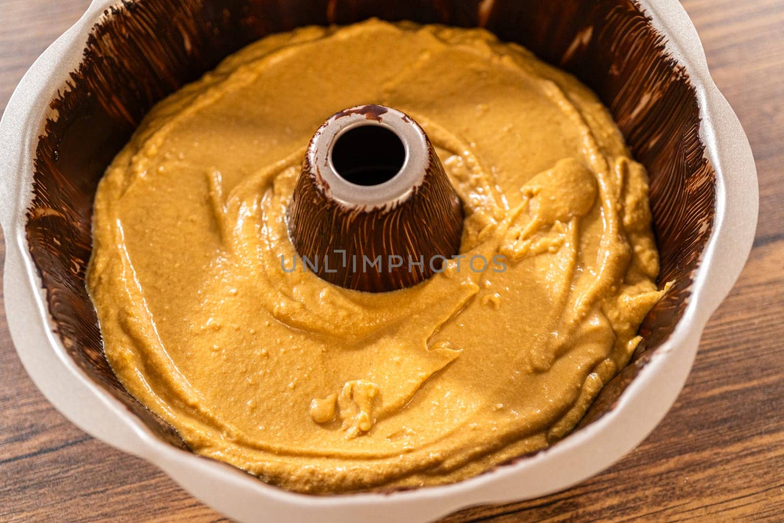 Pouring the gingerbread cake batter into the greased bundt cake pan, ready for a delightful caramel frosting.