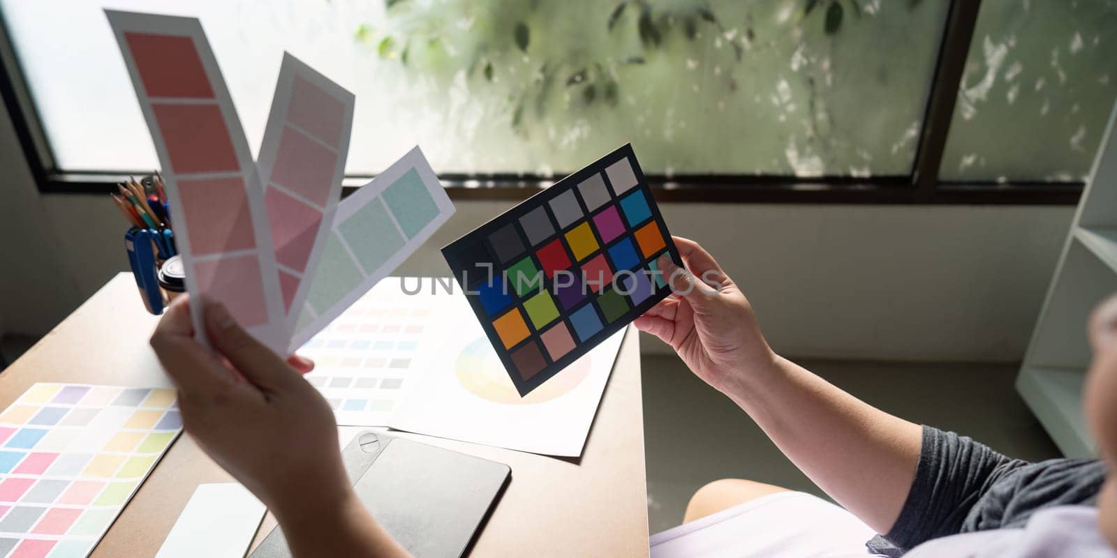 A graphic designer examining color palettes and samples, actively engaged in the design process at a bright and inspiring workspace.