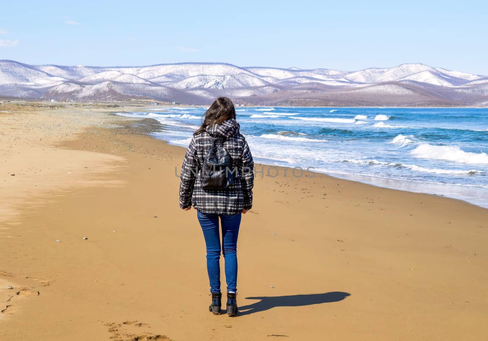 Brunette young woman with backpack walking on the beach close to snowy mountains and Japanese sea. Solo traveller.