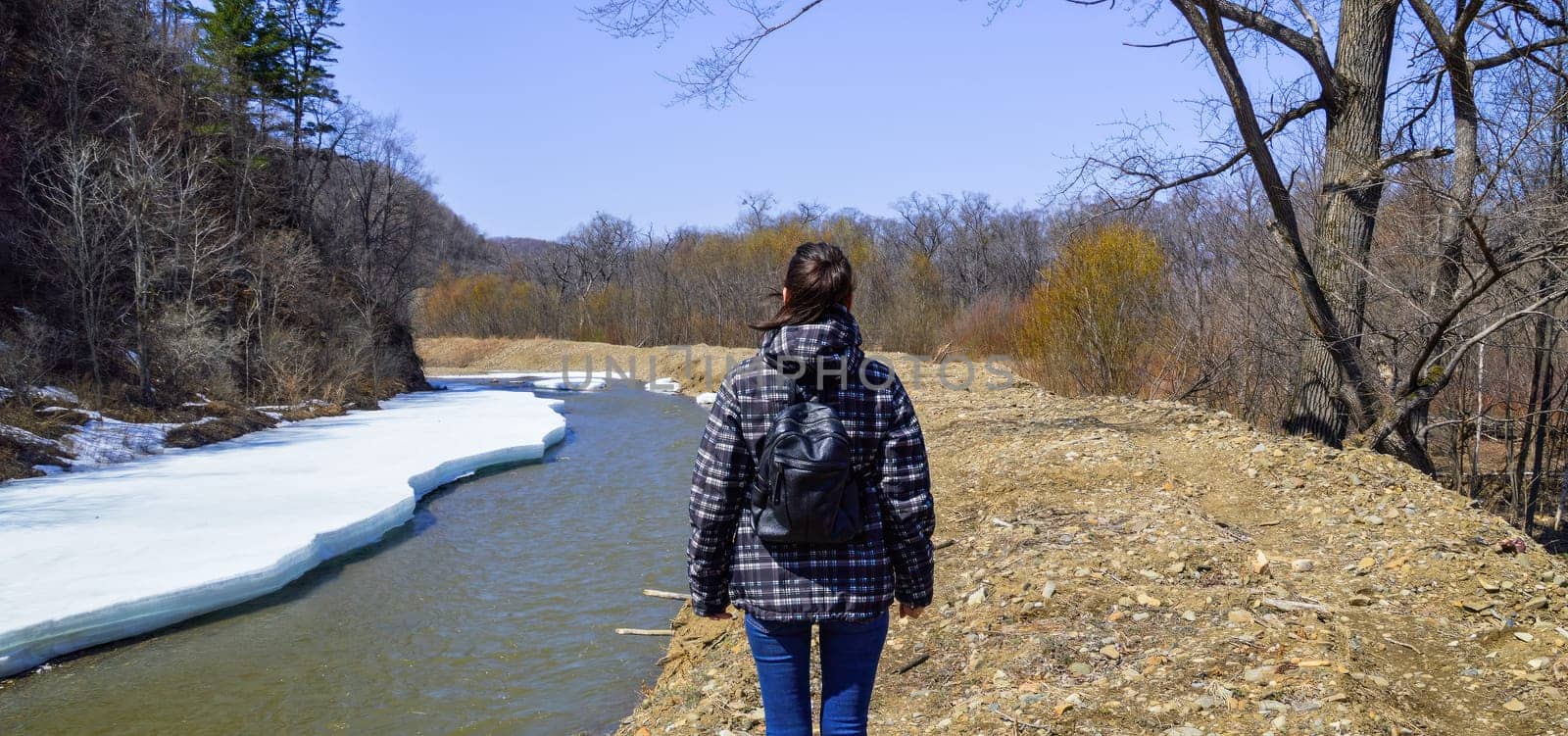 Young brunette woman going camping in the forest next to a melting river with snow on a spring sunny day. Solo traveler