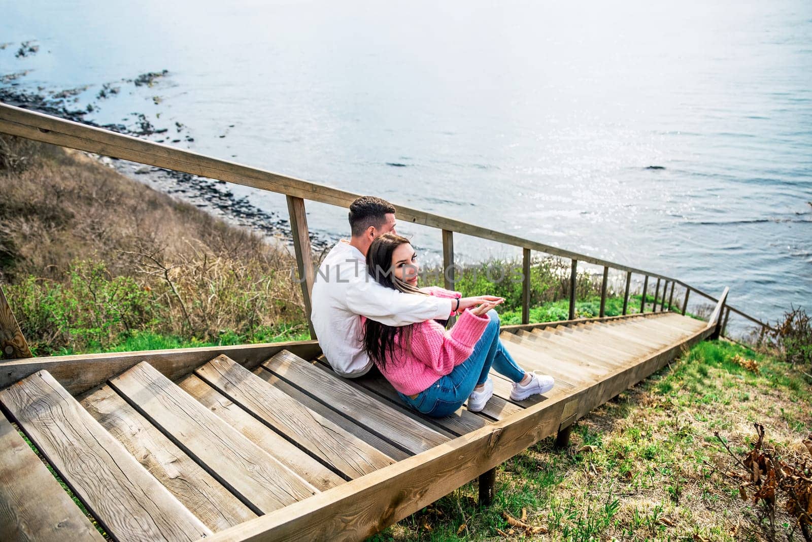 Young married couple sitting on the wooden long stairs and looking at Japanese sea