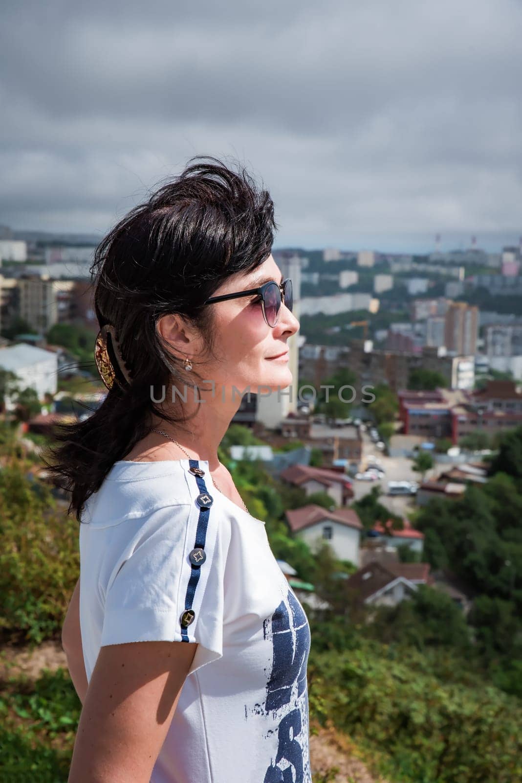 50 years old Russian brunette woman in sunglasses standing against vladivostok city view, portrait