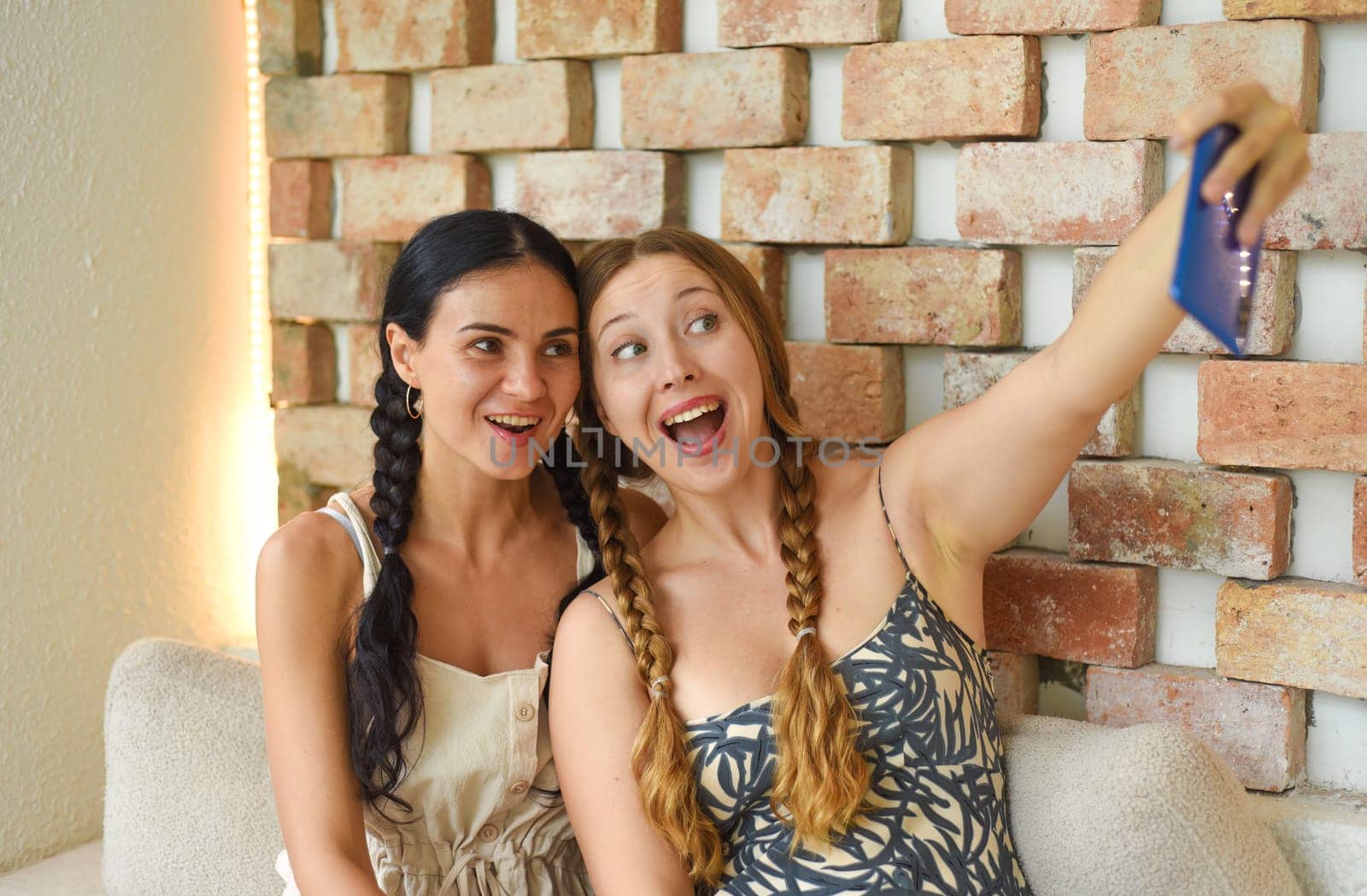Ukrainian woman (brunette) and Russian woman (blonde) portrait together with braids posing and taking a selfie