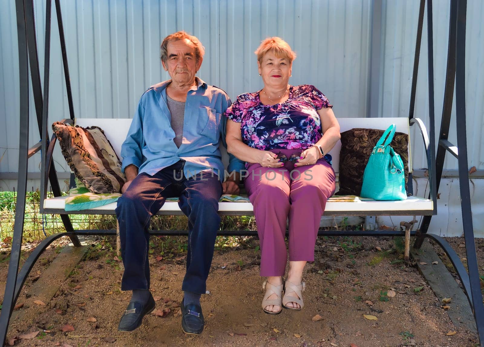 Old Russian married couple sitting on swings together