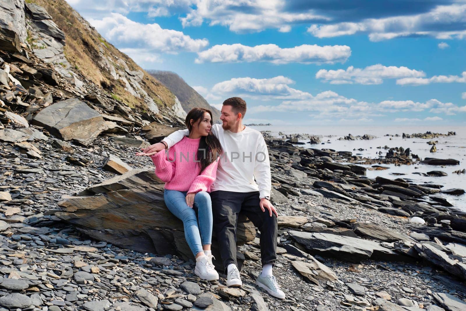 Young russian couple sitting on the stone near Japanese sea on a sunny day
