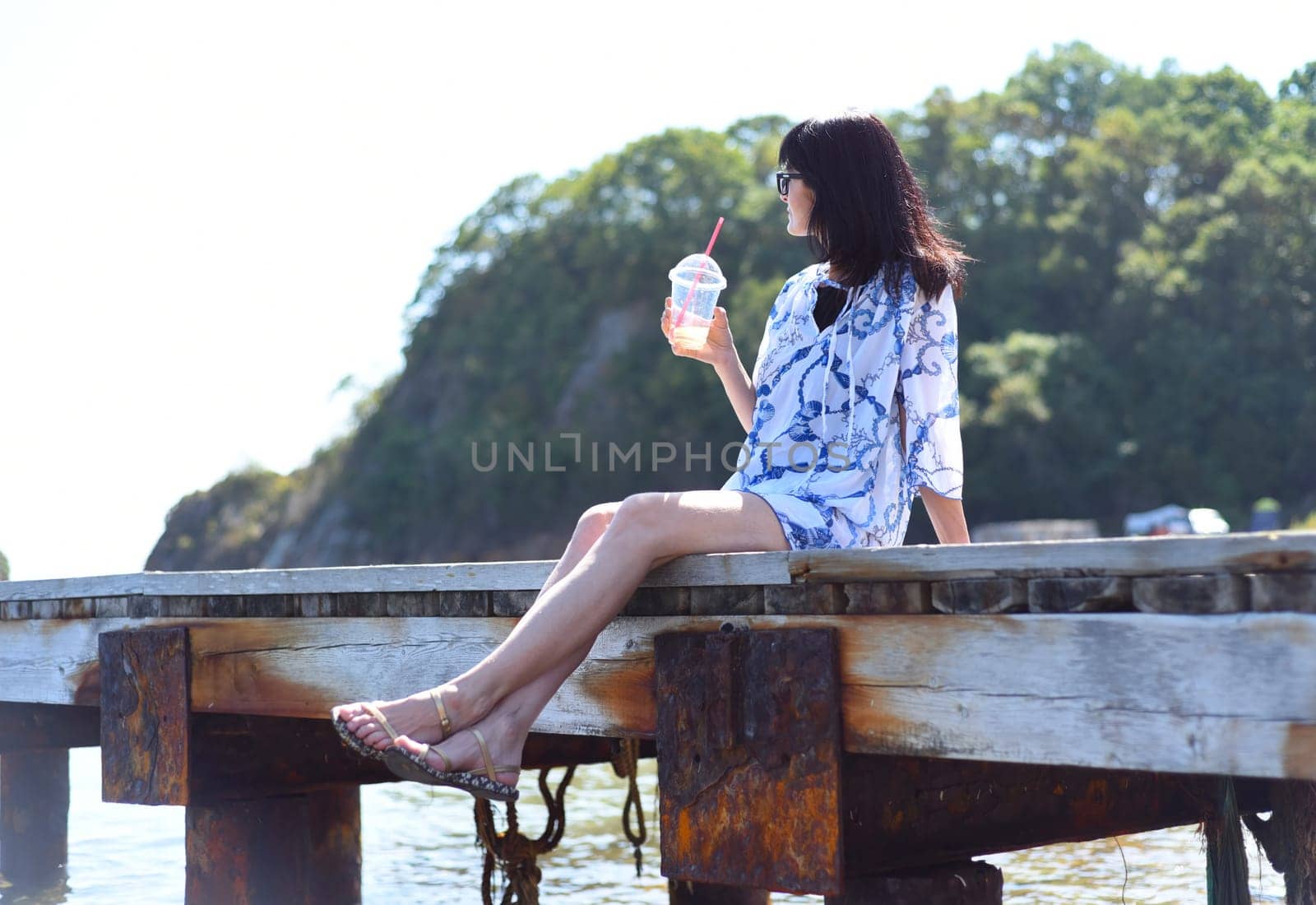 45 years old Russian woman drinking lemonade and sitting on pier