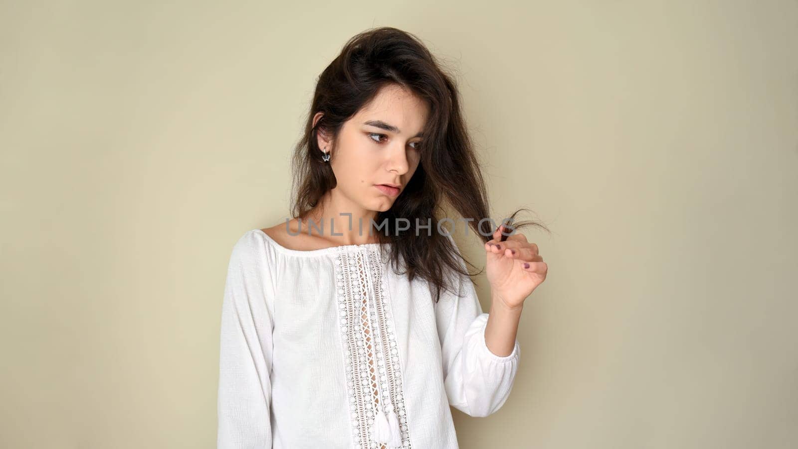 Portrait of young 25 y.o. brunette Russian woman with long hair. In white open shoulder top and looking into the camera on light gray background. Minimum makeup, natural hairstyle. copy space