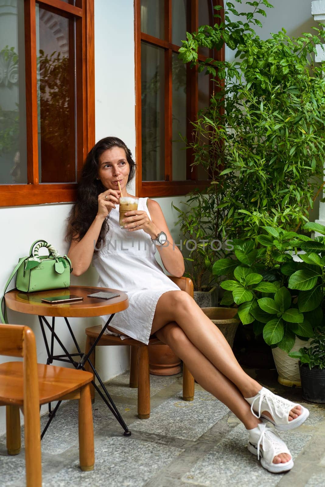Portrait of 39 years old russian woman without make up sitting with glass of ice coffee in white dress
