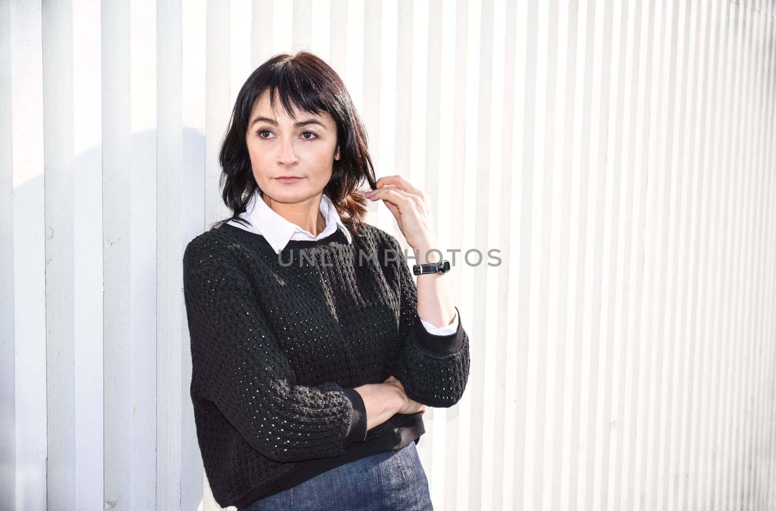 Young brunette woman 45 y.o. standing near a wooden white wall, looking to the side. Copy space
