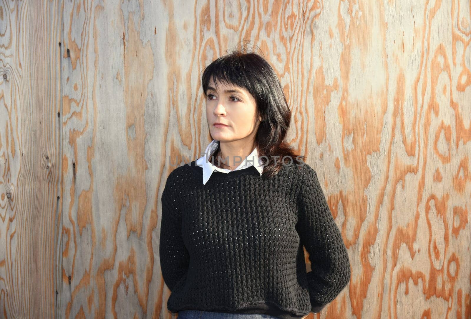 Young beautiful Russian woman in black sweater looking away and standing against the wooden wall. She is serious and confident