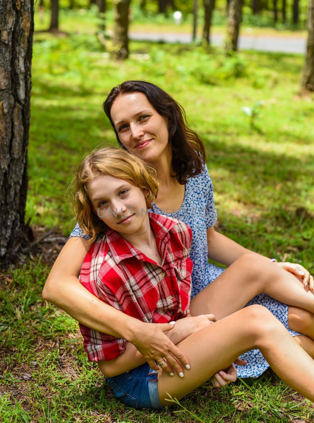 Mother hugging her little daughter resting on her sholder with closed eyes against of green grass in the forest