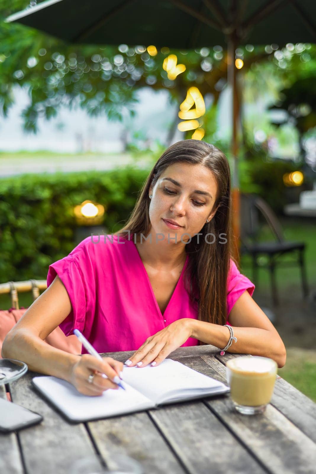 Cute woman sitting on a chair in summer garden and writing in a notebook