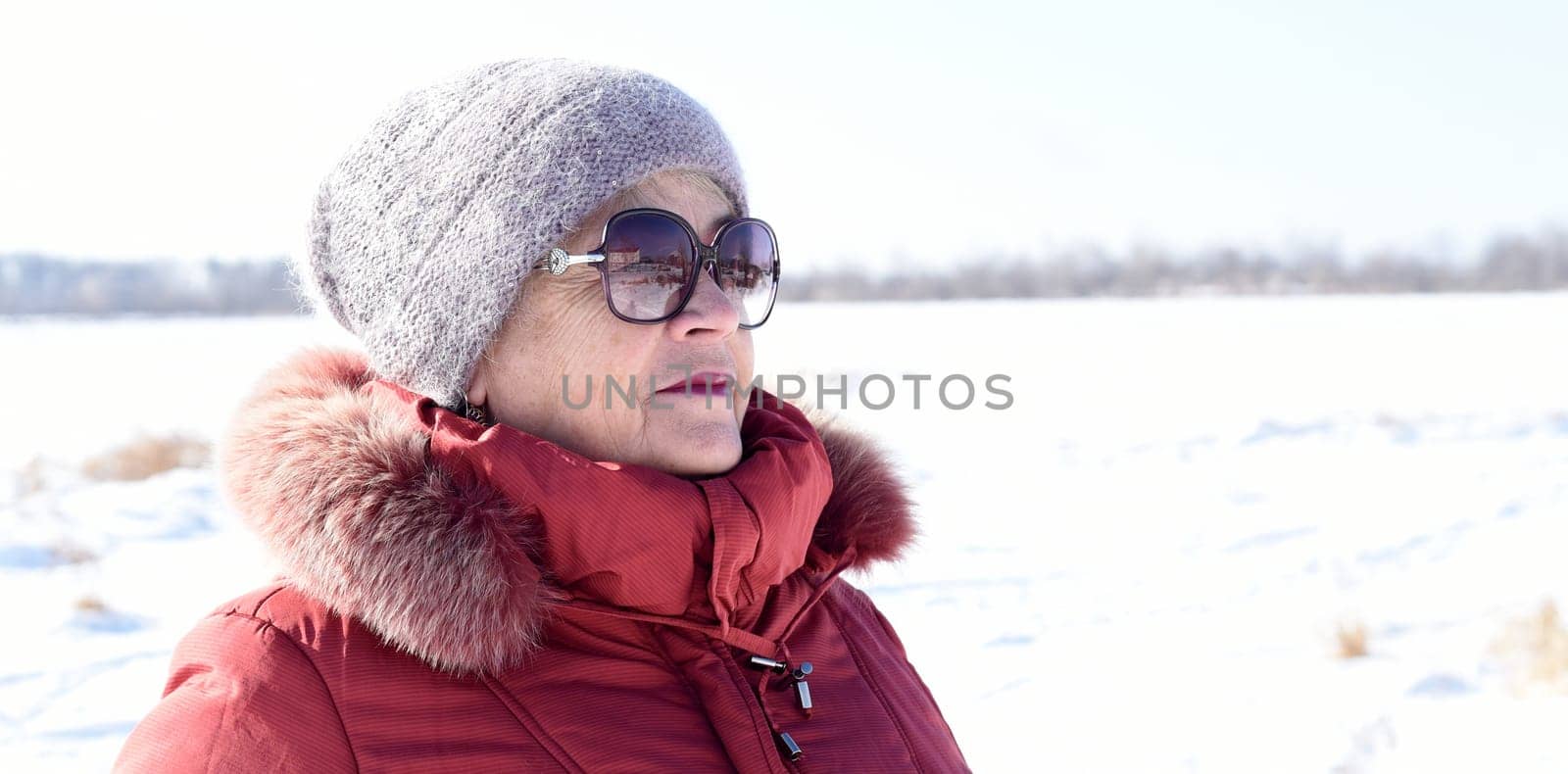 Russian senior woman talking on phone against snowy field. winter