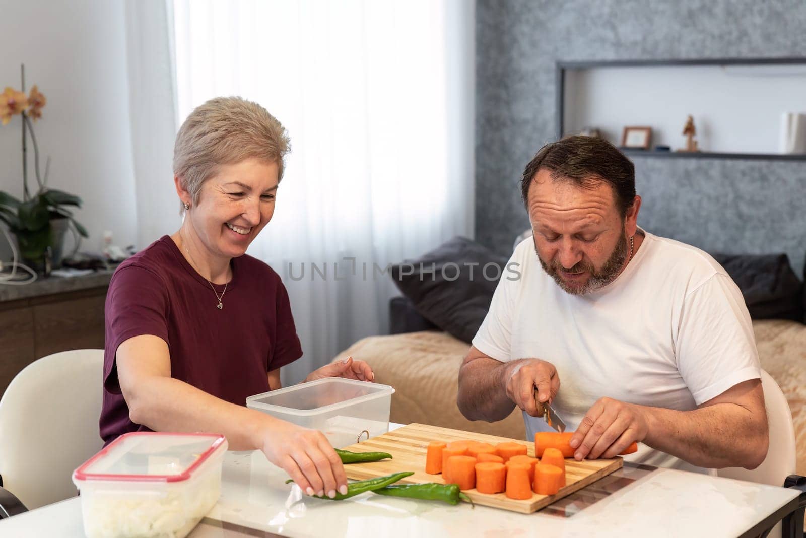 Mature russian husband and wife cooking pilaf together in the kitchen at home