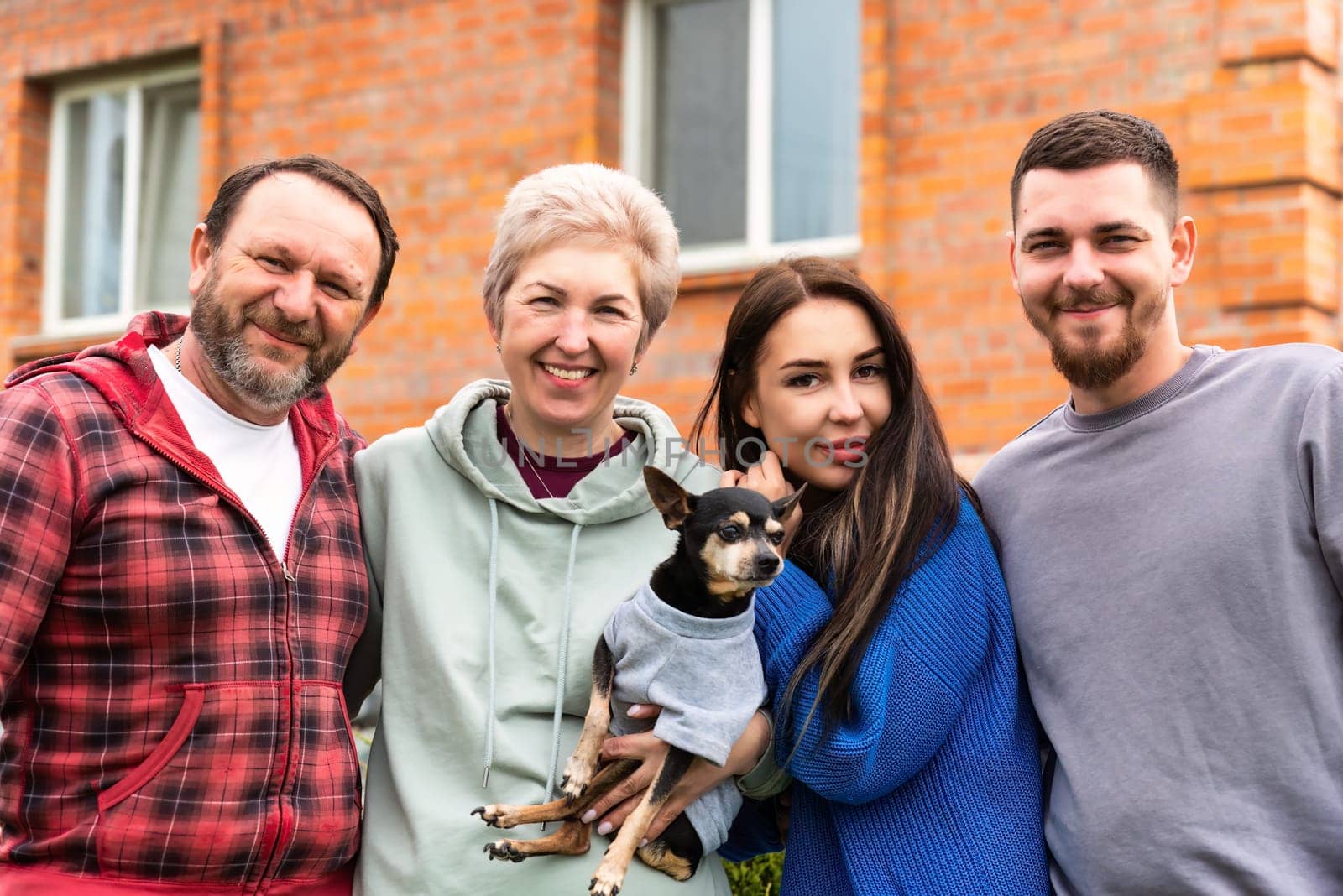 Portrait of happy family together with dog hugging near their  house.